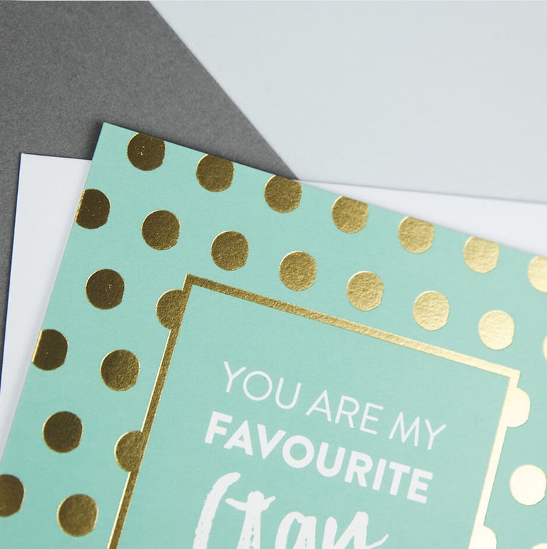 Pu&ograve; includere: Un biglietto di colore azzurro chiaro con pois dorati e un bordo bianco. Il testo all'interno del bordo recita "You are my favourite" con la parola "class" scritta in un grande carattere corsivo.