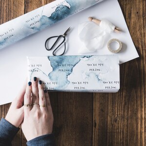 Puede incluir: Un papel de regalo blanco con dise&ntilde;os azules como de acuarela y el texto repetido "You're my person."