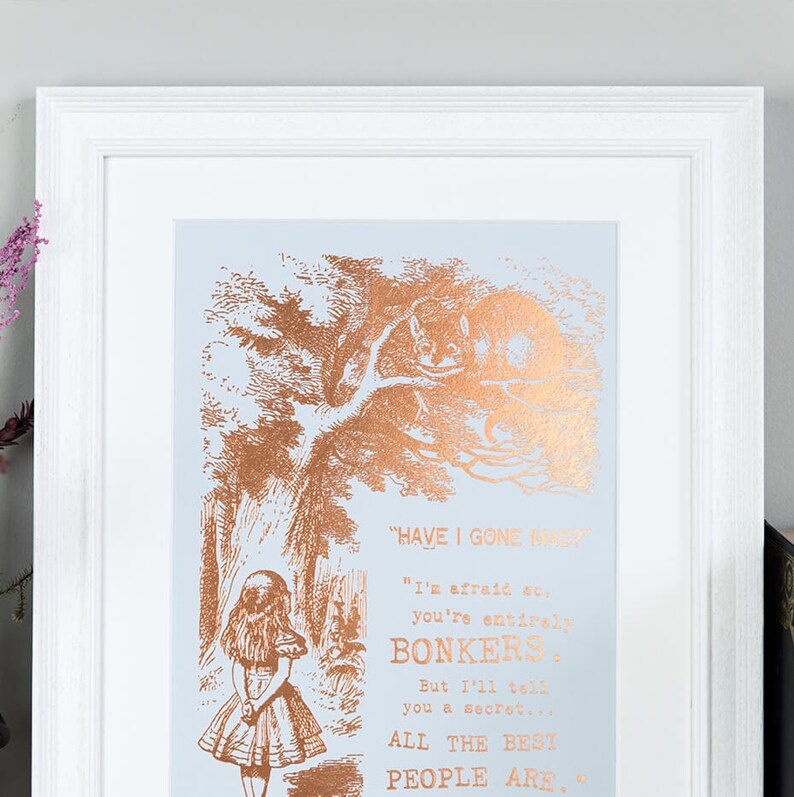 May include: A framed print with a copper foil design of a scene from Alice in Wonderland. The text reads "Have I gone mad?" "I'm afraid so, you're entirely bonkers. But I'll tell you a secret... All the best people are."