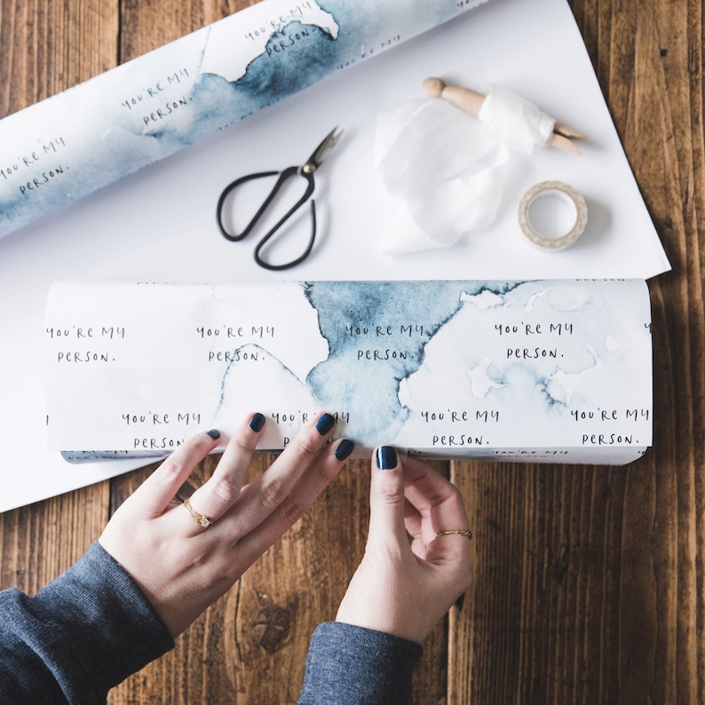 Puede incluir: Un rollo de papel de regalo blanco con un dise&ntilde;o de acuarela azul y el texto "You're my person." repetido en toda la superficie.