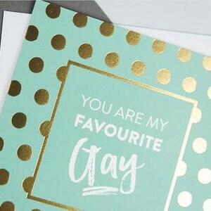 Pu&ograve; includere: Un biglietto azzurro chiaro con pois dorati e il testo "Sei il mio giorno preferito" in lettere bianche.