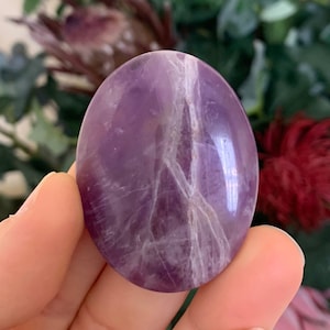 May include: A smooth, polished purple amethyst crystal in the shape of an egg. The crystal has white veins running through it.
