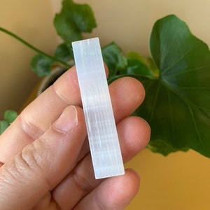 May include: A white selenite stick, also known as a cleansing wand, is a smooth, rectangular piece of crystal. It has a natural, striated texture.