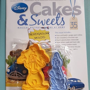May include: A magazine cover featuring Disney's Cakes & Sweets, issue 35. The cover features a photo of a plastic bag containing two yellow and blue cookie cutters shaped like Pluto and Goofy. The text "NERDGASUM MOLDS" is visible on the cover.