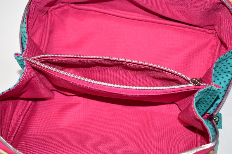 Puede incluir: Vista abierta de un neceser rosa brillante con un bolsillo con cremallera. El interior es de color rosa liso y el exterior presenta tela turquesa con lunares azules. La bolsa est&aacute; dise&ntilde;ada para guardar maquillaje y productos de belleza.