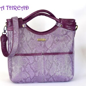 May include: A purple handbag with a snakeskin pattern, featuring a shoulder strap and top handles. The bag has a rectangular shape with a front pocket and a gold-colored rectangular label. The text "ON A THREAD" is visible at the top.