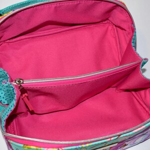 Puede incluir: Bolso de viaje abierto con interior rosa brillante. El bolso tiene un exterior turquesa con un estampado de lunares y cierre de cremallera. Tiene un asa y un peque&ntilde;o bolsillo interior. Medidas no disponibles.