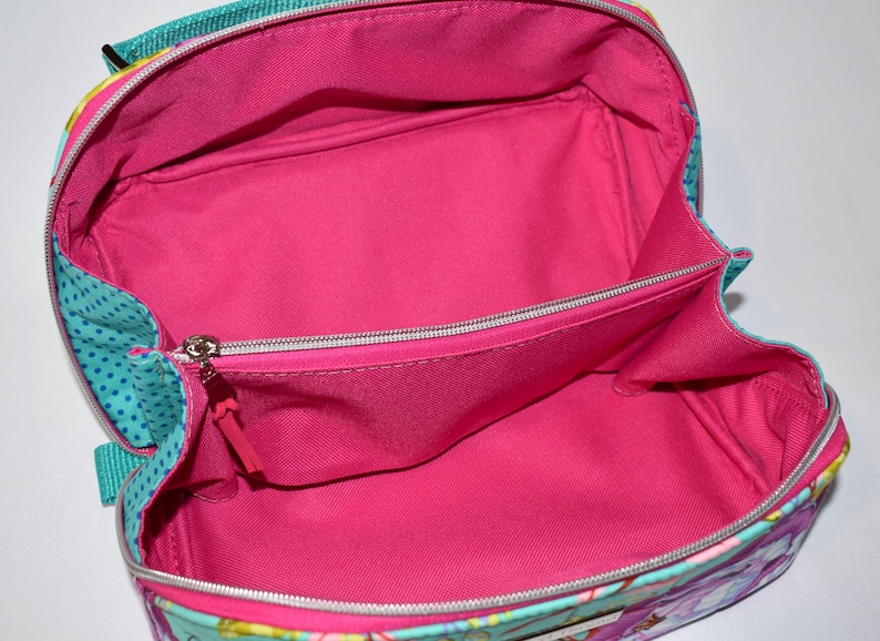 Puede incluir: Bolso de viaje abierto con interior rosa brillante. El bolso tiene un exterior turquesa con un estampado de lunares y cierre de cremallera. Tiene un asa y un peque&ntilde;o bolsillo interior. Medidas no disponibles.