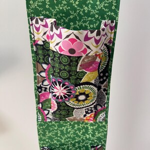 May include: A green fabric organizer with multiple pockets. The pockets feature a floral pattern with pink, purple, yellow, and white flowers on a dark green background. The organizer's exterior is a lighter green with a small floral pattern.