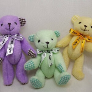 May include: Three small teddy bears, one purple, one green, and one yellow, each with a ribbon around their neck. The purple bear has a white ribbon with the text "treasure" on it. The green bear has a white ribbon with the text "Teddy Love" on it. The yellow bear has a yellow ribbon with the text "Teddy Love" on it.