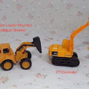 May include: Two toy construction vehicles, a yellow wheel loader with a hydraulic breaker attachment and a yellow excavator with a black track base. The wheel loader has the word "CULES" printed on the side. The excavator has the text "PC TH600 POWER" printed on the side.
