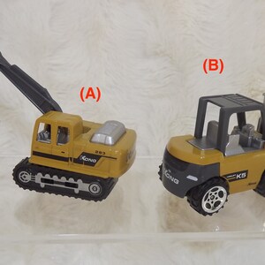 K&ouml;nnte beinhalten: Zwei Spielzeug-Baumaschinen, ein gelber Bagger mit einem schwarzen Arm und ein gelber Gabelstapler mit einer grauen Kabine. Beide Fahrzeuge haben schwarze Reifen und den Text "XONG" an der Seite.