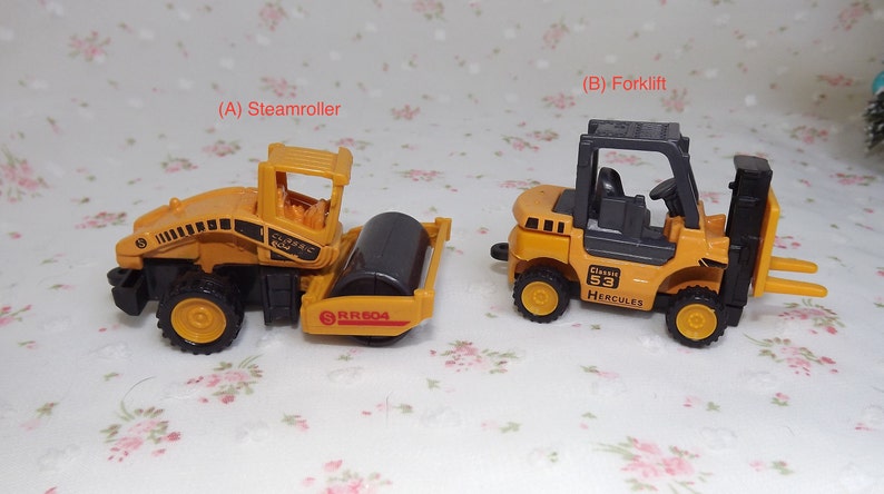 May include: Two toy construction vehicles, a yellow steamroller with a black roller and a yellow forklift with a black cab. The steamroller has the text "RR604" on the side and the forklift has the text "Classic 53 Hercules" on the side.