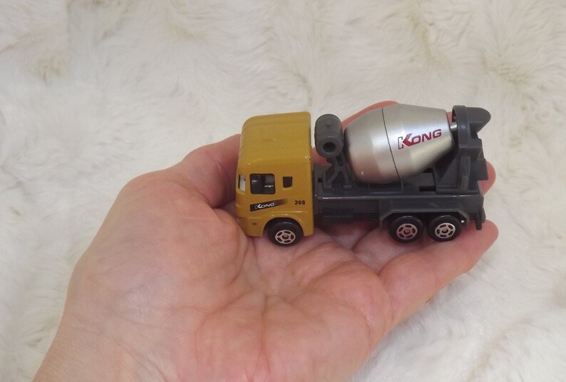 K&ouml;nnte beinhalten: Ein gelber Spielzeug-Betonmischer mit einem silbernen rotierenden Trommel. Der LKW hat den Schriftzug "KONG" auf der Seite der Trommel.