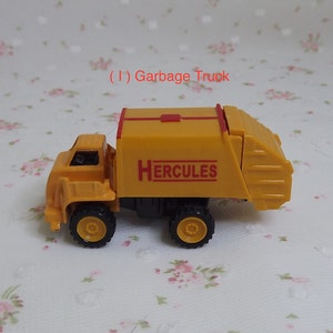 May include: Yellow toy garbage truck with a red stripe and the word "HERCULES" printed on the side.