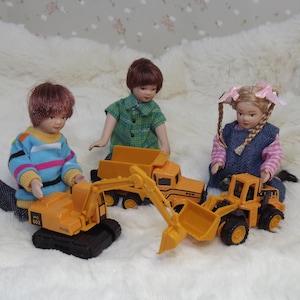 May include: Three children play with toy construction vehicles. A girl in a blue and white dress holds a yellow toy dump truck. A boy in a blue and pink striped shirt holds a yellow toy excavator. A girl in a green and white plaid shirt holds a yellow toy dump truck.
