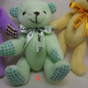 May include: Three plush teddy bears with different colored fur and patterned fabric. The bear on the left is purple with brown and white checkered fabric. The middle bear is green with green and white checkered fabric. The bear on the right is yellow with yellow and white checkered fabric. Each bear has a ribbon tied around its neck with a message on it.