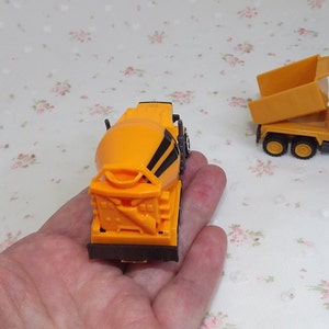 May include: Two toy construction trucks, one is a yellow dump truck with a raised bed and the other is a yellow cement mixer truck.