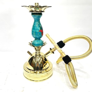 Puede incluir: Una cachimba dorada con una columna central de mosaico turquesa y rojo. La cachimba tiene una manguera dorada y una parte superior decorativa. La base es redonda y tiene un diseño escalonado.