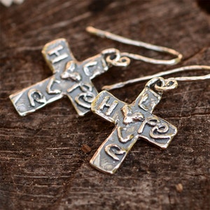May include: A pair of silver cross earrings with a textured finish. The crosses have the word "Hope" inscribed on them.