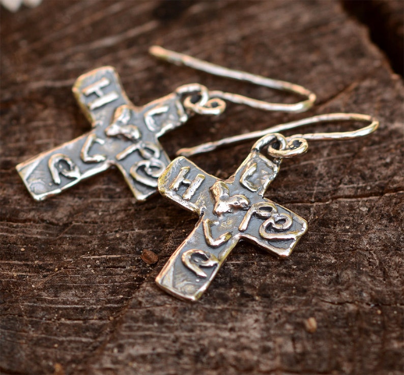 May include: A pair of silver cross earrings with a textured finish. The crosses have the word "Hope" inscribed on them.