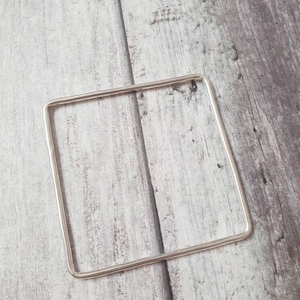 May include: A silver square bangle bracelet. The bracelet is made of a single piece of metal that is bent into a square shape.