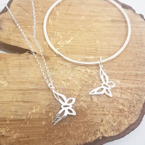 May include: A silver necklace with a butterfly pendant and a matching silver bangle bracelet. The butterfly pendant and charm have a cut-out design. The jewelry is displayed on a wooden surface.