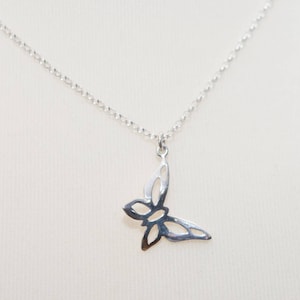 May include: A silver-colored butterfly pendant necklace. The butterfly pendant is a cutout design, and the necklace chain is a delicate, linked style. The necklace is displayed against a neutral background.