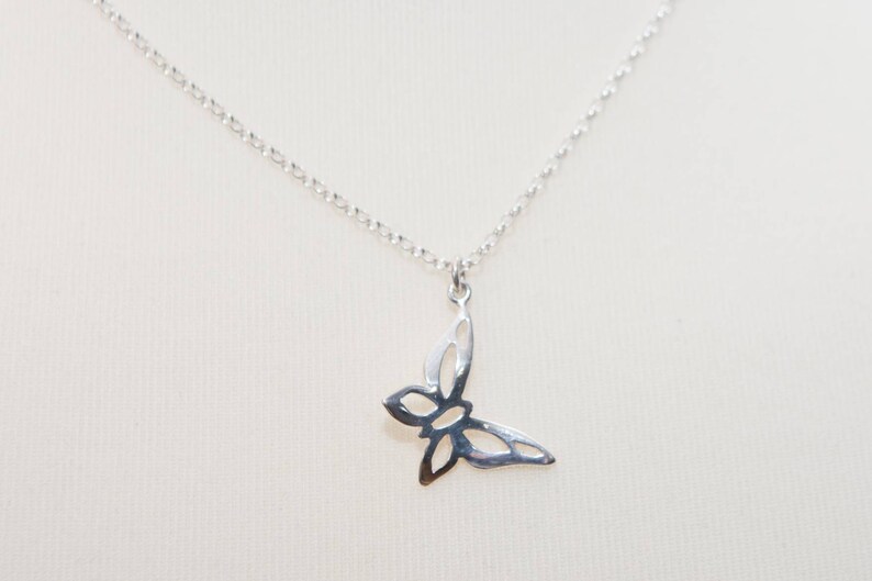 May include: A silver-colored butterfly pendant necklace. The butterfly pendant is a cutout design, and the necklace chain is a delicate, linked style. The necklace is displayed against a neutral background.