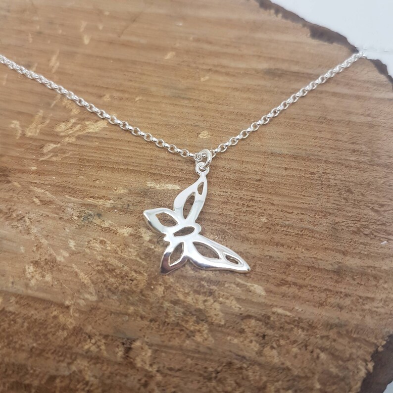 May include: A silver butterfly pendant necklace. The pendant features a detailed butterfly design with openwork wings. The necklace chain is delicate and silver. The necklace is displayed on a wooden surface.