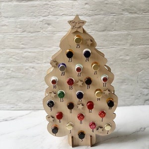 May include: Wooden Christmas tree advent calendar with 25 numbered compartments for small bottles. The tree is decorated with small stars and the text "Making Spirits Bright".