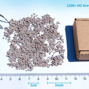 May include: A pile of over 1200 small grey plastic bricks, measuring approximately 2.5 cm in length, for model railroading. The bricks are packaged in a brown cardboard box with the text "1200+ Tiny Bricks by.naaron88" printed on the side.