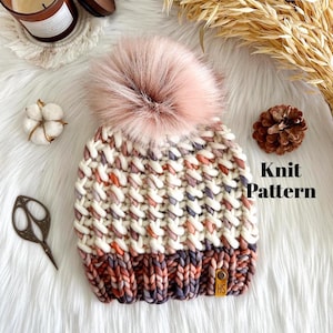 May include: A knitted hat with a pink pom pom, featuring a white and multi-colored striped pattern with a solid colored band at the bottom. The hat has a brown leather tag with the letters "HS" on it. The text "Knit Pattern" is visible in the image.