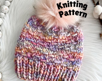 May include: A colorful knitted beanie with a fluffy pink pom pom. The beanie has a multi-colored yarn with shades of pink, purple, orange, and yellow. The beanie has a leather tag with the letters "HS" on it. Knitting Pattern.