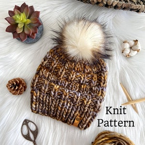 May include: Knit hat pattern featuring a brown, purple, and gold yarn with a white pom pom. The hat is on a white fuzzy surface with a ball of yarn, a small pine cone, a succulent, and a pair of scissors.
