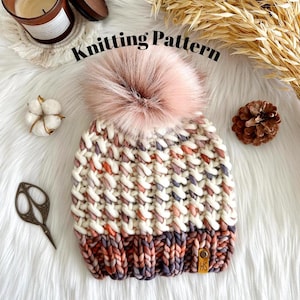 May include: Knitting pattern for a white and pink beanie with a fluffy pom pom. The beanie has a textured stitch pattern and a brown leather tag with the letters "HS" on it.
