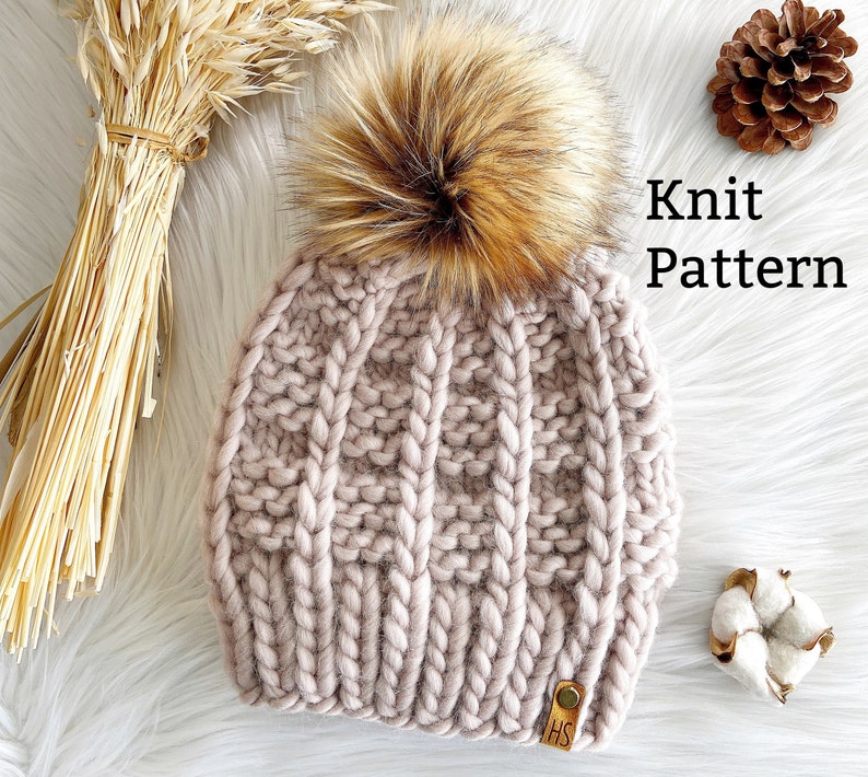 May include: A knitted hat with a fluffy brown pom pom. The hat is a light pink color and has a cable knit pattern. The hat is labeled "Knit Pattern".