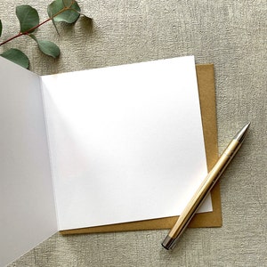 May include: A blank white card with a brown envelope and a gold pen. The card is folded in half and the envelope is open.