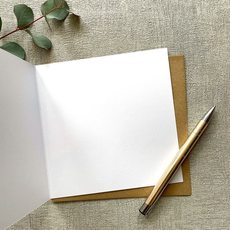 May include: A blank white card with a brown envelope and a gold pen. The card is folded in half and the envelope is open.