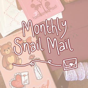 May include: A stationery set featuring a sticker sheet with a brown teddy bear, a rose in a glass bottle, and a heart-shaped envelope. The text Monthly Snail Mail is printed in white. Includes a dark red envelope and a spool of light pink twine.