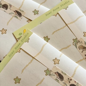 May include: Multiple cream-colored envelopes featuring a repeating pattern of light green stars and wavy gold lines. Each envelope is sealed with decorative adhesive tape displaying illustrations of hedgehogs and the text Scar Rose Studio.