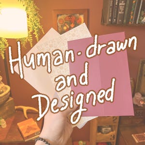 May include: A set of folded greeting cards featuring a solid mauve card and a white card with a delicate, repeating floral line art pattern. The text "Human-drawn and Designed" is overlaid in a bold, white, hand-lettered font across the cards.