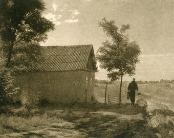 May include: A black and white photograph of a person walking away from a small, one-story house with a corrugated metal roof. The person is carrying a bag over their shoulder and is walking on a dirt path. There are trees in the background.