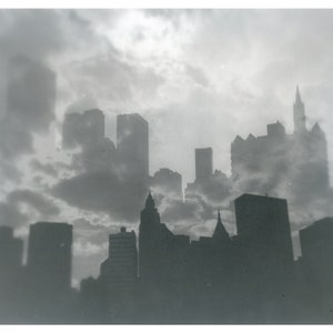 May include: A black and white photograph of a city skyline with tall buildings obscured by clouds. The buildings are silhouetted against the cloudy sky.
