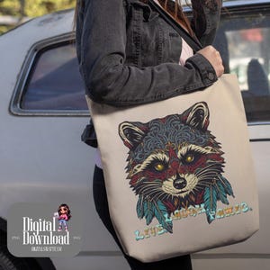 Puede incluir: Bolso tote beige con una ilustración detallada de un mapache con intrincados patrones en tonos azules, rojos y turquesas. El mapache tiene ojos amarillos y plumas turquesas. El texto "LIVE LAUGH PANIC" está impreso en azul claro.