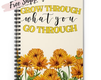 May include: A spiral bound notebook with a cream colored cover and yellow flowers at the bottom. The text "GROW THROUGH what you GO THROUGH" is printed in black on the cover.