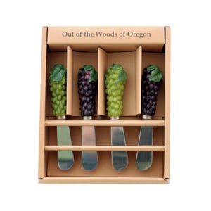 May include: Set of four stainless steel cheese spreaders with green and purple grape handles. The spreaders are packaged in a brown cardboard box with the text "Out of the Woods of Oregon" printed on the top.