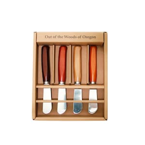 May include: Set of five wooden handled butter knives in a cardboard box. The box is labeled "Out of the Woods of Oregon". The knives have different colored wooden handles, including brown, red, and natural wood.