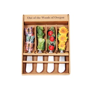 May include: Set of five decorative butter knives in a cardboard box. The knives feature colorful designs of butterflies, frogs, ladybugs, and sunflowers. The box is labeled "Out of the Woods of Oregon".