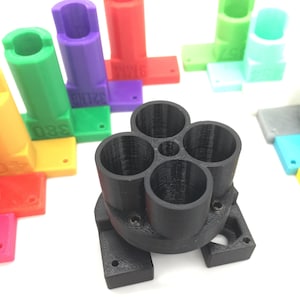 May include: A black 3D printed holder with four round openings for holding items. Two small silver metal pins are on a white surface.